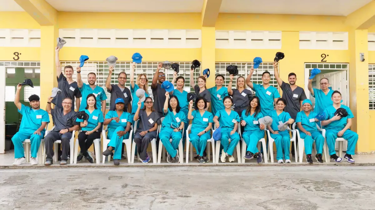 Envista volunteers happily posing while raising Envista caps in the air.
